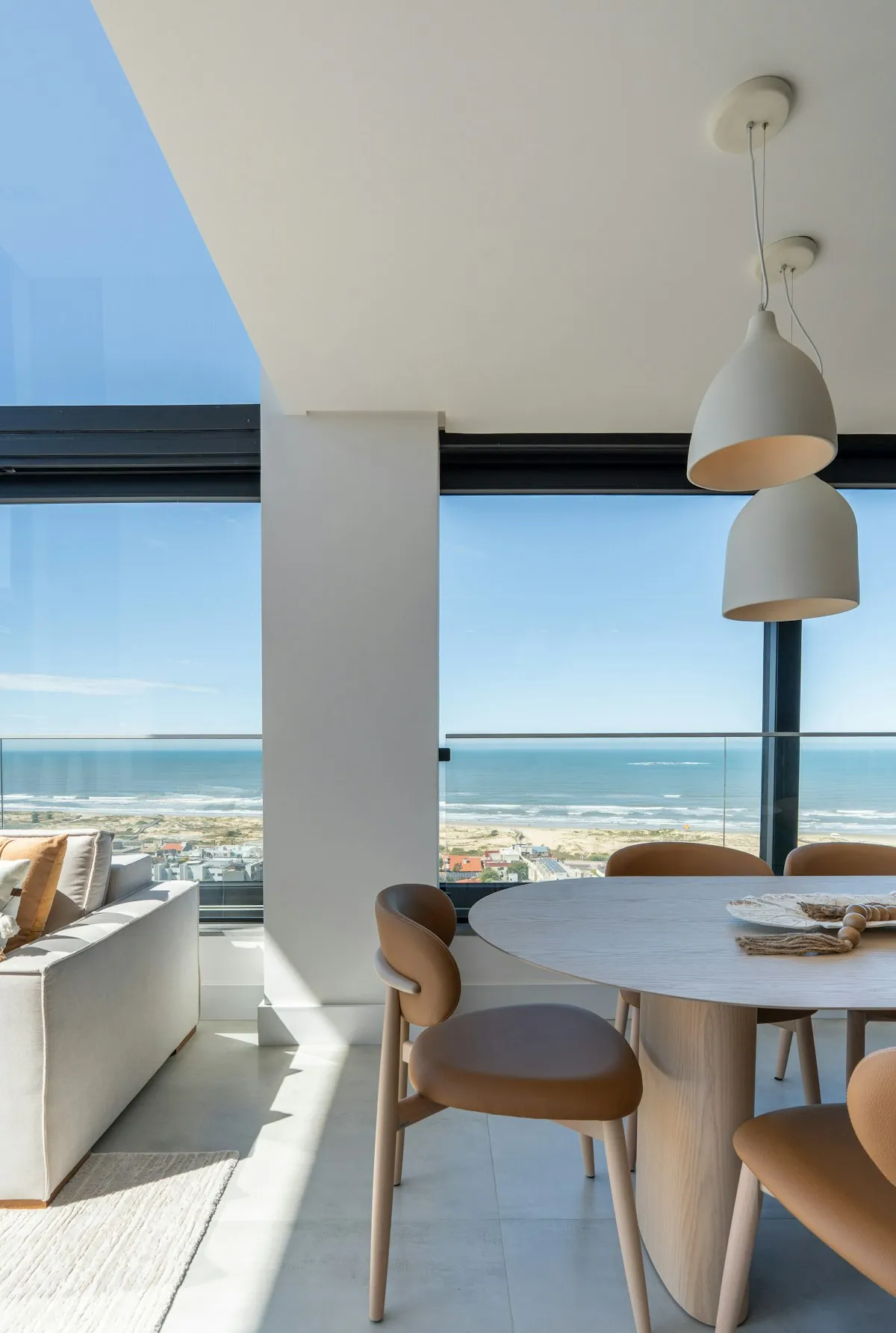 Sala de jantar clara com janelas do piso ao teto e vista para o mar