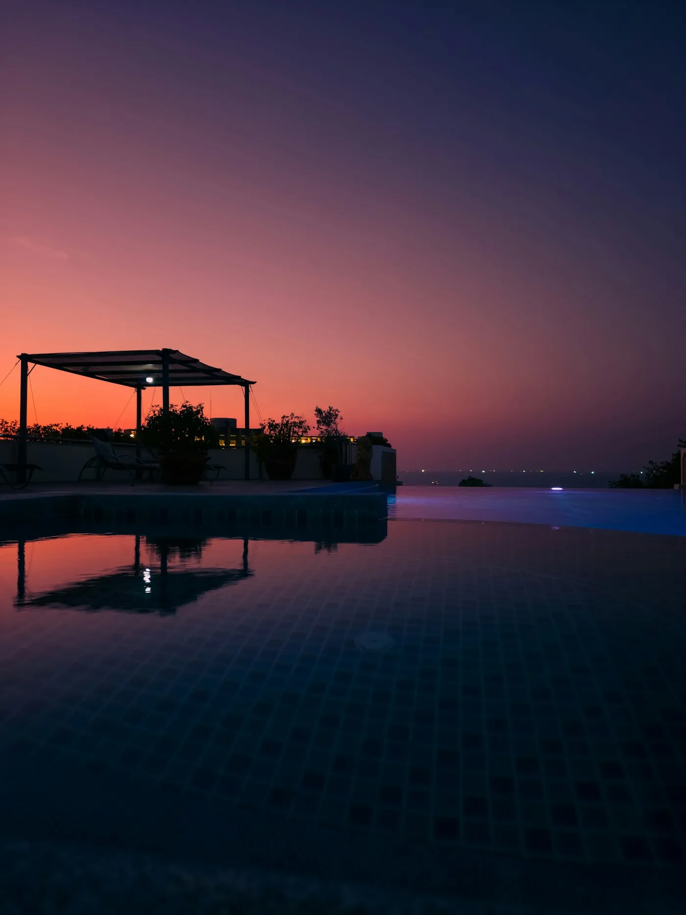 Piscina de borda infinita refletindo o céu rosado do entardecer