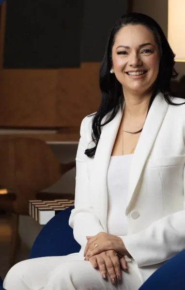 A mentora da Rêvo sorrindo, de terninho branco, sentada numa poltrona azul